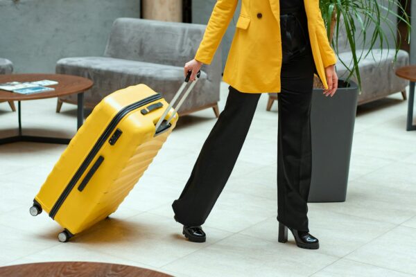 Stylish woman walking in hotel lobby pulling a bright yellow suitcase.